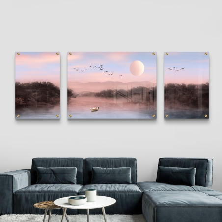 סט שלוש תמונות זכוכית מחולקות המציגות נוף פסטלי עם סירה במים, עצים, הרים, שמש וצללית של ציפורים, תלוי מעל ספה מודרנית בסלון.          Ask ChatGPT