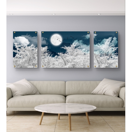שלישיית תמונות קנבס מחולקות המציגות נוף לילי עם עצים מושלגים, ירח מלא בשמים כהים וציפורים עפות, תלויה מעל ספה מודרנית בעיצוב מינימליסטי.          Ask ChatGPT