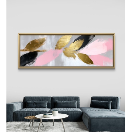 תמונת קנבס פנורמית עם עלים מופשטים בגווני ורוד, שחור וזהב על רקע אפור תלויה מעל ספה אפורה בסלון מודרני.