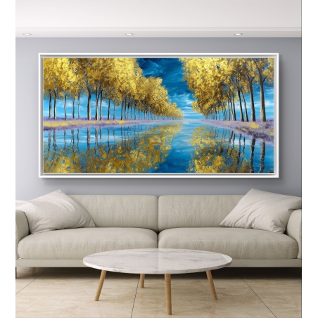 תמונת קנבס לרוחב המציגה שורת עצים זהובים המשתקפים באגם כחול, תלויה מעל ספה כהה בעיצוב מודרני.