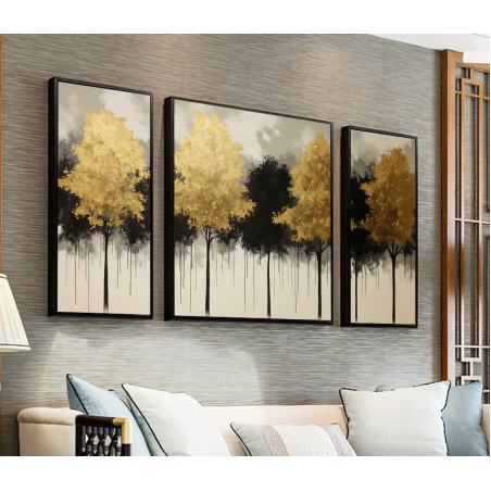 שלוש תמונות קנבס מחולקות המציגות עצים בגווני זהב ושחור על רקע בהיר, תלויות בסלון מעוצב עם קירות בגוון אפור בהיר.
