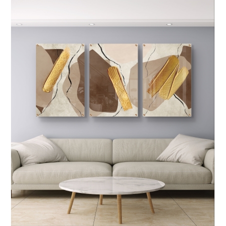 שלישיית תמונות זכוכית מופשטות עם משיחות זהב בגווני בז' וחום, תלויה מעל ספה בצבע שמנת בסלון מודרני.