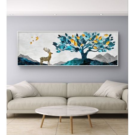 תמונת קנבס פנורמית של צבי מוזהב לצד עץ בעל עלים בטורקיז וזהב על רקע הרים, תלויה מעל ספה בהירה בחלל סלון מודרני.