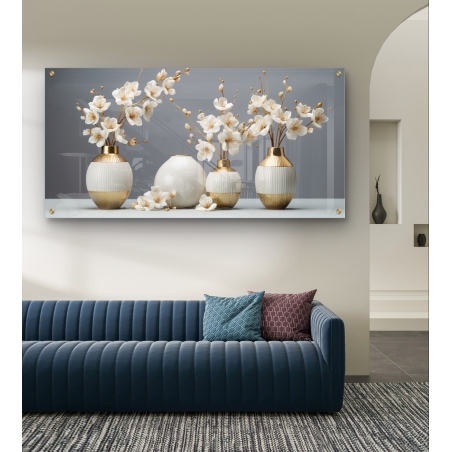תמונת זכוכית לרוחב עם אגרטלים מעוצבים בגווני זהב ולבן ופרחים לבנים, תלויה מעל ספה כחולה בסלון מודרני.