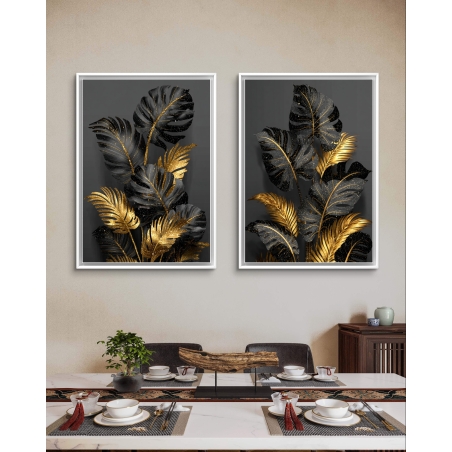 זוג תמונות קנבס עם עלים בגווני שחור וזהב על רקע אפור, תלויות מעל שולחן אוכל בעיצוב מודרני ויוקרתי.