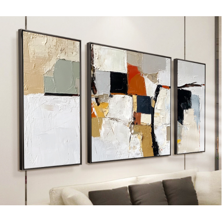 שלישיית תמונות קנבס בעיצוב מופשט, מחולקות עם גוונים של לבן, שמנת, אפור, ונגיעות כתומות ושחורות, משלימות חלל מגורים בעיצוב מודרני.