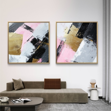 זוג תמונות קנבס מרובעות מופשטות בגווני ורוד, שחור, לבן וזהב תלויות על קיר אפור מעל ספה בהירה בסלון מודרני עם שולחן שיש עגול.