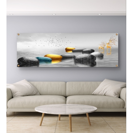 תמונה פנורמית מודרנית על זכוכית עם אבנים עגולות במים בצבעי שחור, זהב וטורקיז, זוג איילים מוזהבים וציפורים בשמיים, תלויה מעל ספה בהירה.