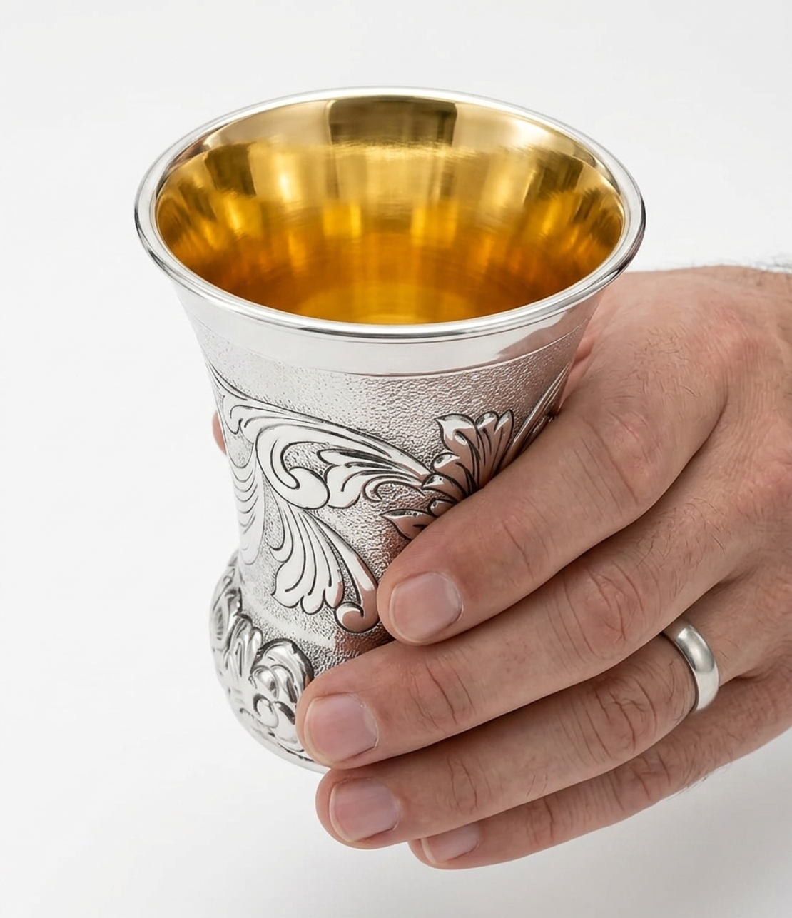 A hand holding a unique and decorated Kiddush cup made of pure silver