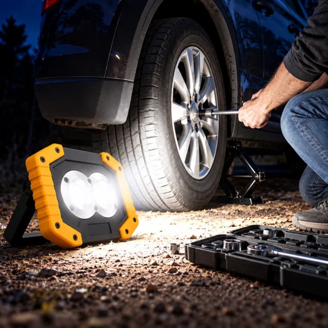 פרוז'קטור נייד נטען GoodMix עם תאורת LED עוצמתית, מאיר את אזור הגלגל בזמן החלפת גלגל ברכב בשעות הלילה.