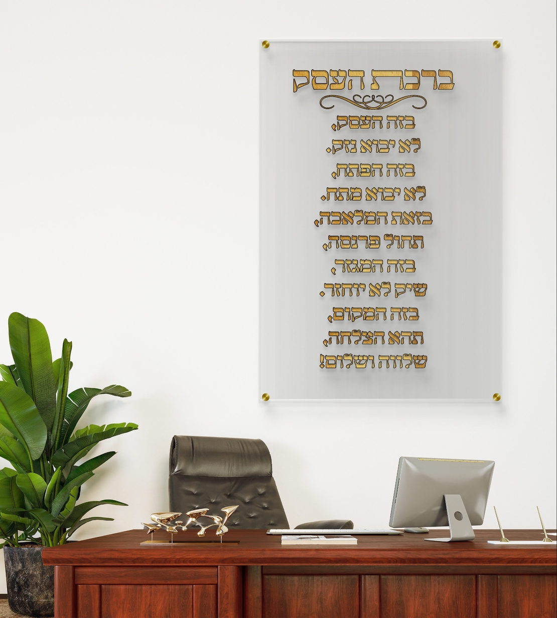 תמונת זכוכית שקופה עם כיתוב מוזהב של ברכת העסק תלויה על קיר לבן במשרד מודרני עם שולחן עץ כהה וכסא מנהלים.