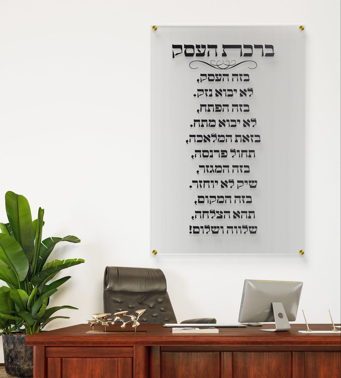 תמונת זכוכית שקופה עם כיתוב ברכת העסק בצבע שחור תלויה על קיר לבן במשרד יוקרתי עם שולחן עץ כהה, כסא מנהלים וצמח ירוק בצד.
