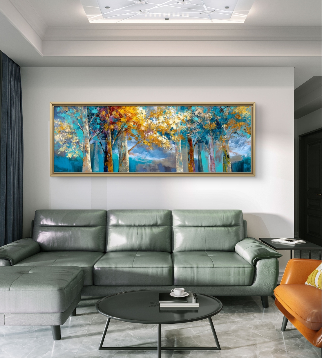 תמונת קנבס פנורמית של יער בגווני טורקיז וזהב מעל ספה אפורה.