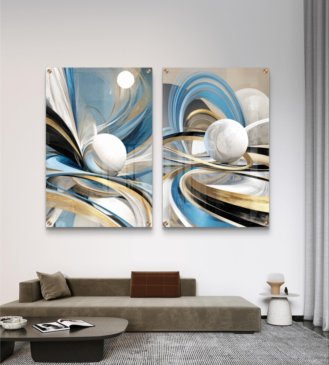 סט תמונות זכוכית זוג בעיצוב אבסטרקטי עם קווים זורמים בגווני כחול, תכלת וזהב וכדורים לבנים תלת מימדיים מעל ספה מודרנית.