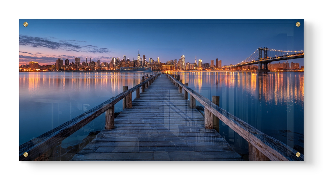 תמונת זכוכית בהדפסה חלקה של מזח עץ המוביל אל עיר מוארת בלילה עם השתקפויות על המים, בעיצוב מודרני ויוקרתי.