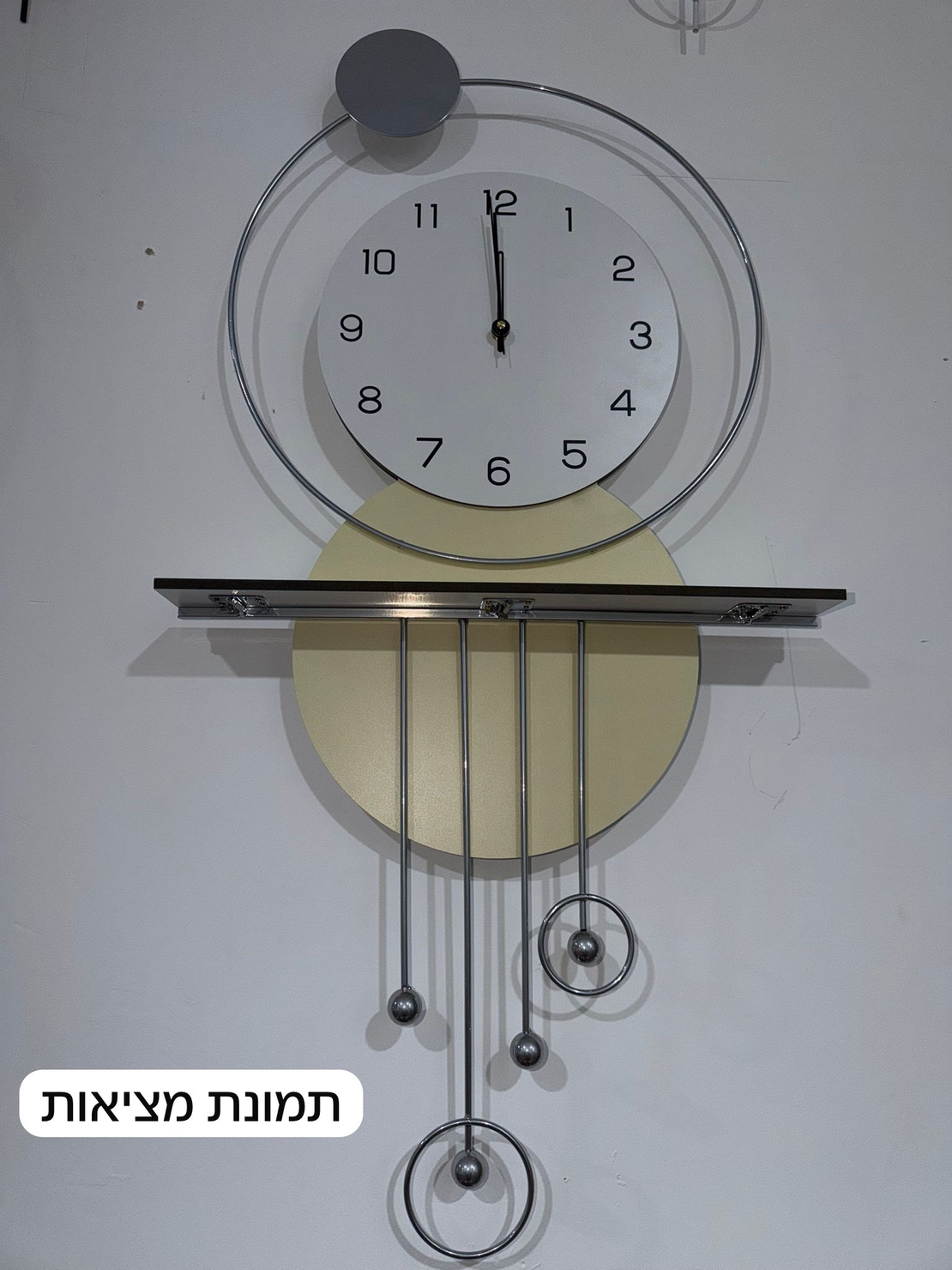 שעון קיר מעוצב בסגנון מודרני עם צורות גיאומטריות, מסגרת עגולה, מטוטלות דקורטיביות וגימור אלגנטי בגווני זהב, אפור ולבן, תלוי על קיר בעיצוב מינימליסטי.