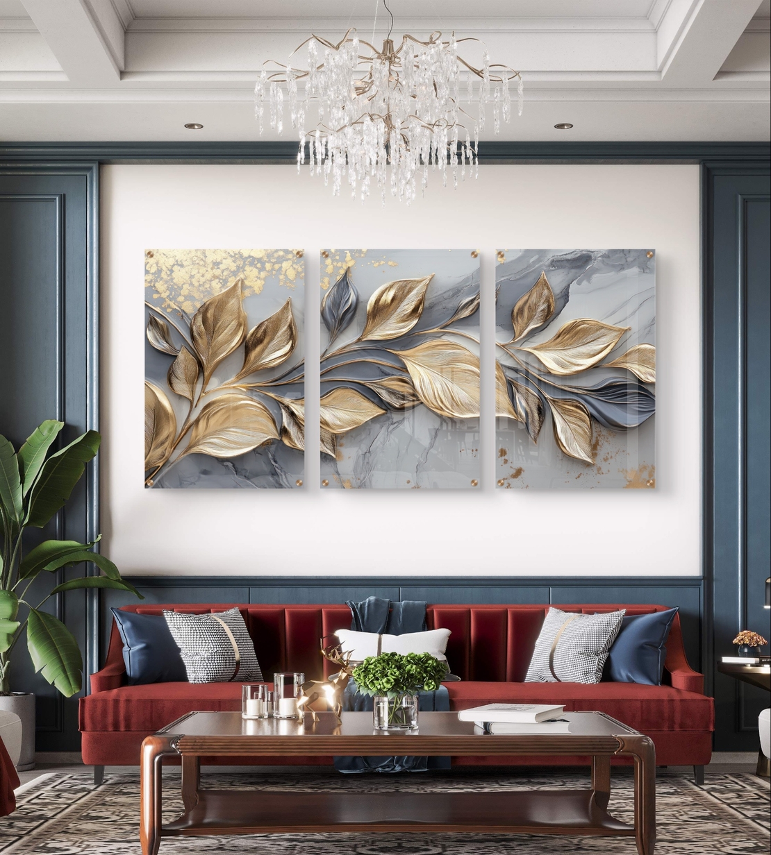 שלישיית תמונות זכוכית עם עלים מוזהבים בתנועה על רקע שיש אפור בעיצוב יוקרתי