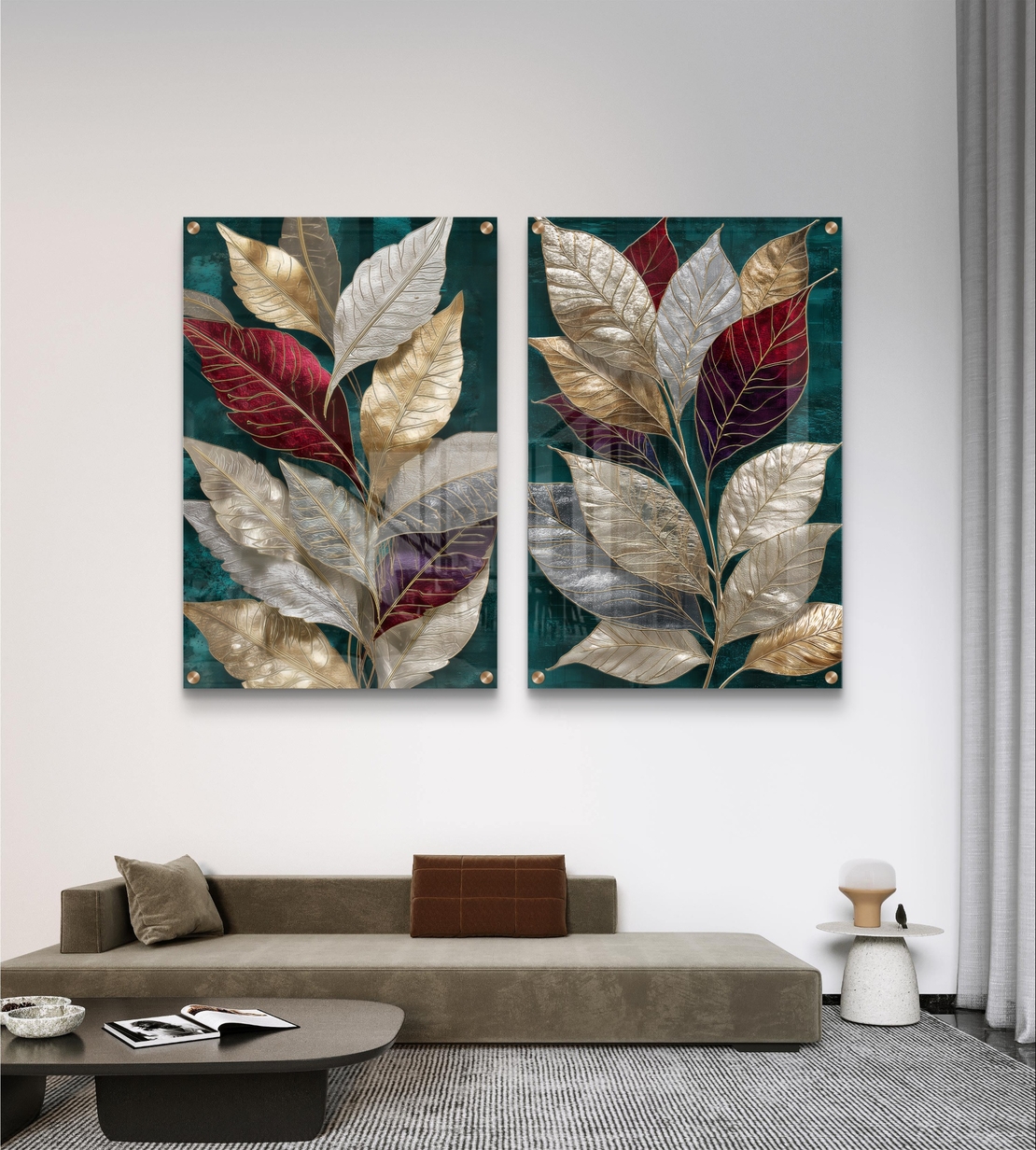 סט תמונות זכוכית זוג עם עלים גדולים בגווני זהב, בורדו ושמנת על רקע ירוק אמרלד תלוי מעל ספה כחולה בסלון מודרני.