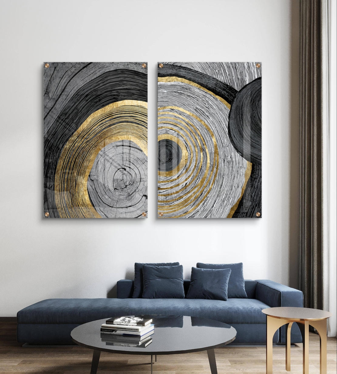 סט תמונות זכוכית זוג בעיצוב אבסטרקטי עם מעגלים קונצנטריים בגווני שחור, אפור ולבן עם נגיעות זהב מעל ספה מודרנית כחולה.