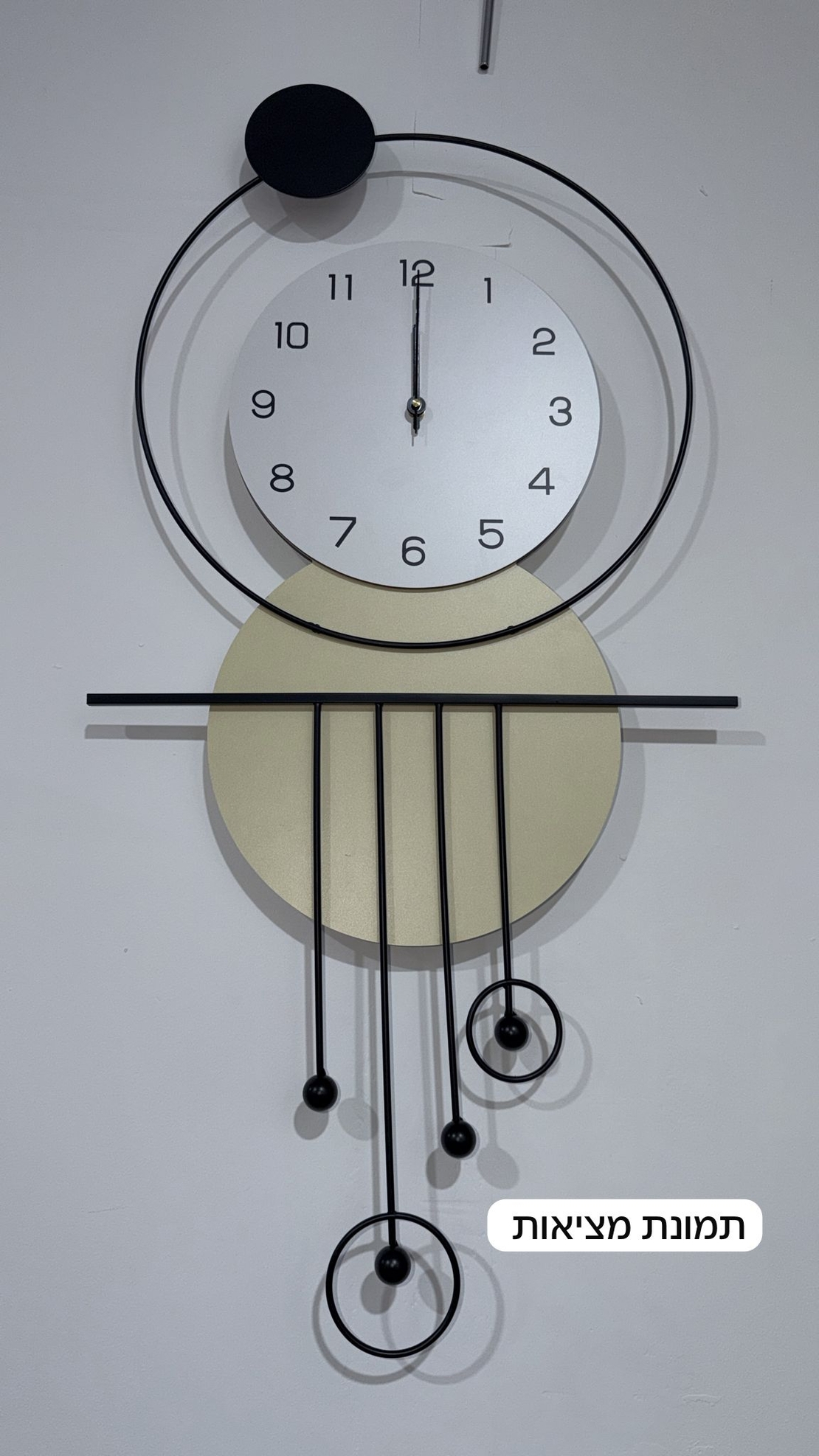 שעון קיר מעוצב בסגנון מודרני עם צורות גאומטריות, מסגרת עגולה, מטוטלות דקורטיביות וגימור אלגנטי בגווני שחור, לבן וזהב, תלוי על קיר בהיר.