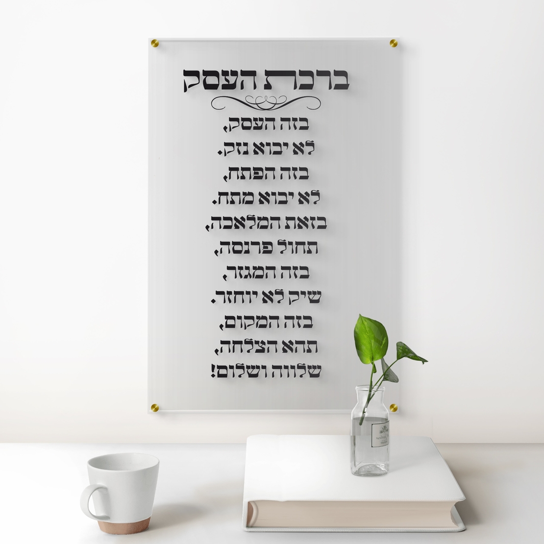 תמונת זכוכית שקופה עם כיתוב ברכת העסק בצבע שחור תלויה על קיר לבן במשרד יוקרתי עם שולחן עץ כהה, כסא מנהלים וצמח ירוק בצד.