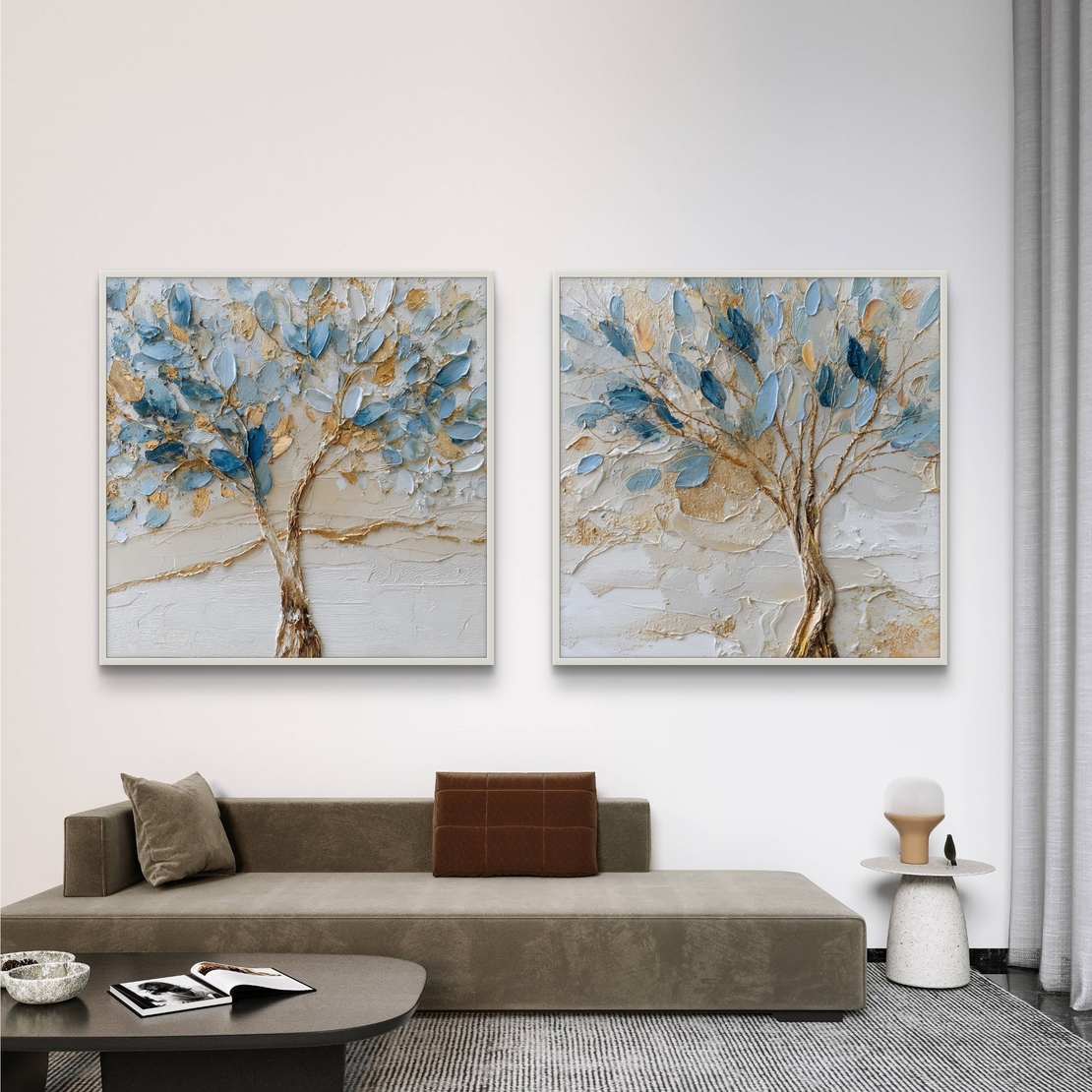 סט זוג תמונות קנבס מרובעות עם עצים אמנותיים בגווני כחול ותכלת ונגיעות זהב על רקע שמנתי, תלויות מעל ספה מודרנית.