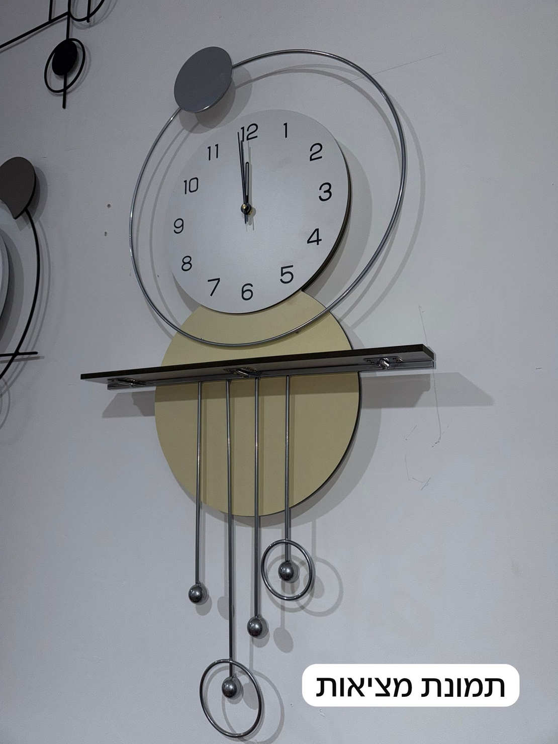 שעון קיר מעוצב בסגנון מודרני עם צורות גיאומטריות, מסגרת עגולה, מטוטלות דקורטיביות וגימור אלגנטי בגווני זהב, אפור ולבן, תלוי על קיר בעיצוב מינימליסטי.