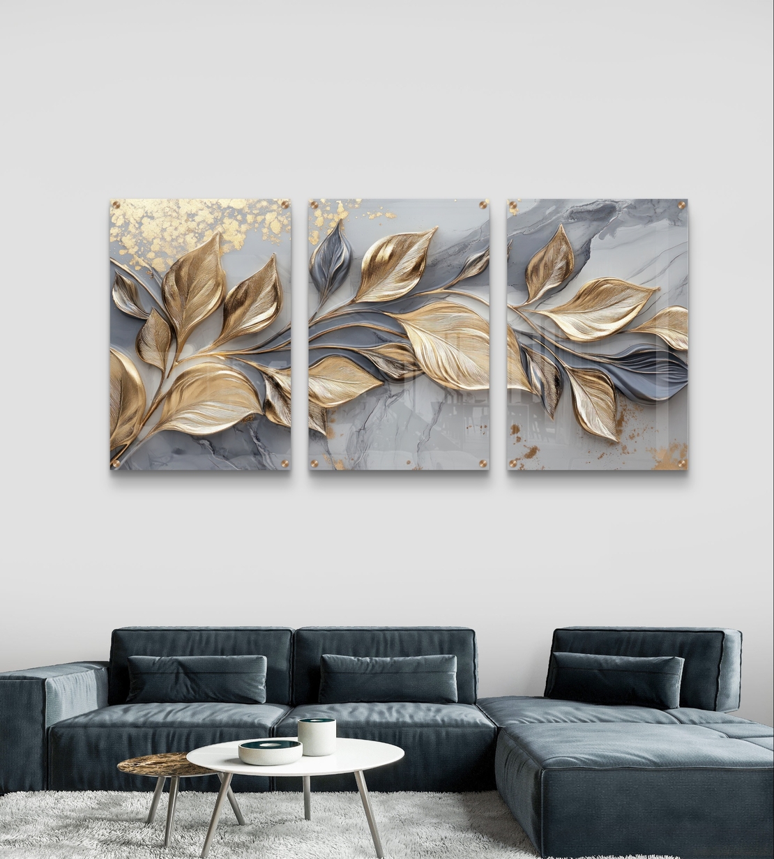 שלישיית תמונות זכוכית עם עלים מוזהבים בתנועה על רקע שיש אפור בעיצוב יוקרתי