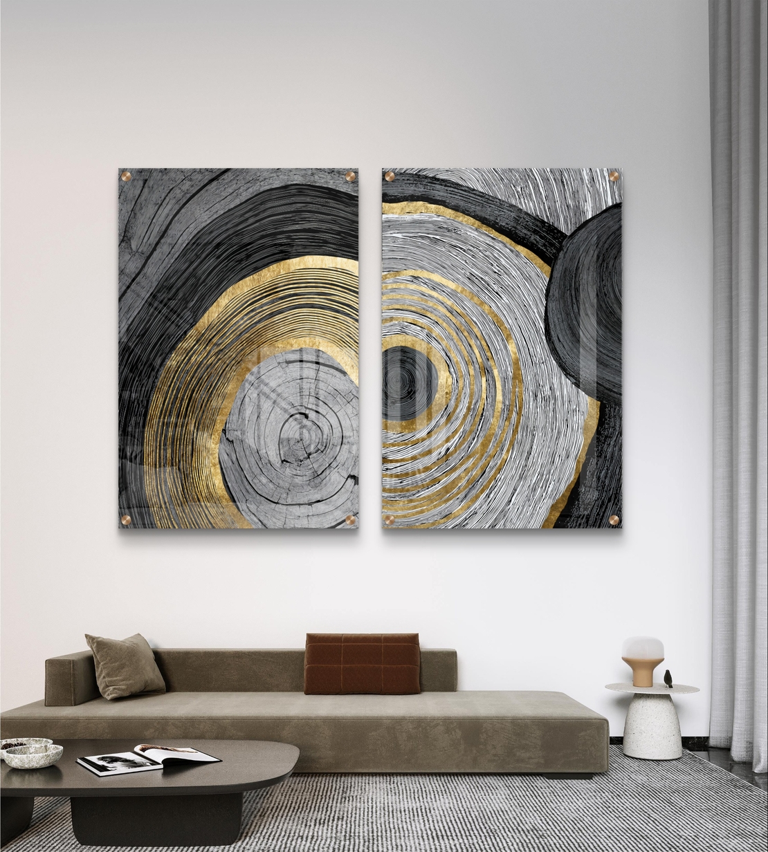 סט תמונות זכוכית זוג בעיצוב אבסטרקטי עם מעגלים קונצנטריים בגווני שחור, אפור ולבן עם נגיעות זהב מעל ספה מודרנית כחולה.